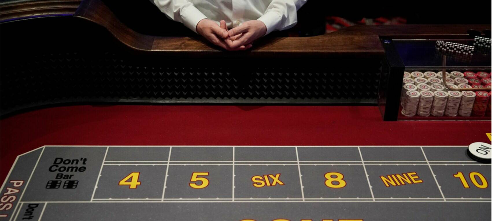 casino dealer with hands folded at craps table